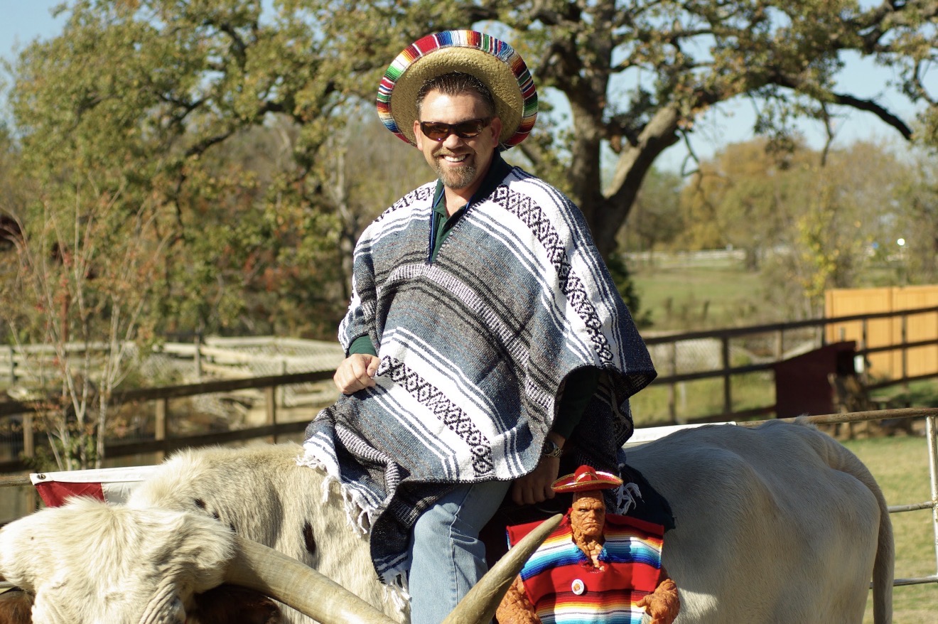 Chuck Dumas wearing a Mexican poncho and sombrero beside a longhorn, showing his humor, adventurous spirit, gratitude, and approachable personality.